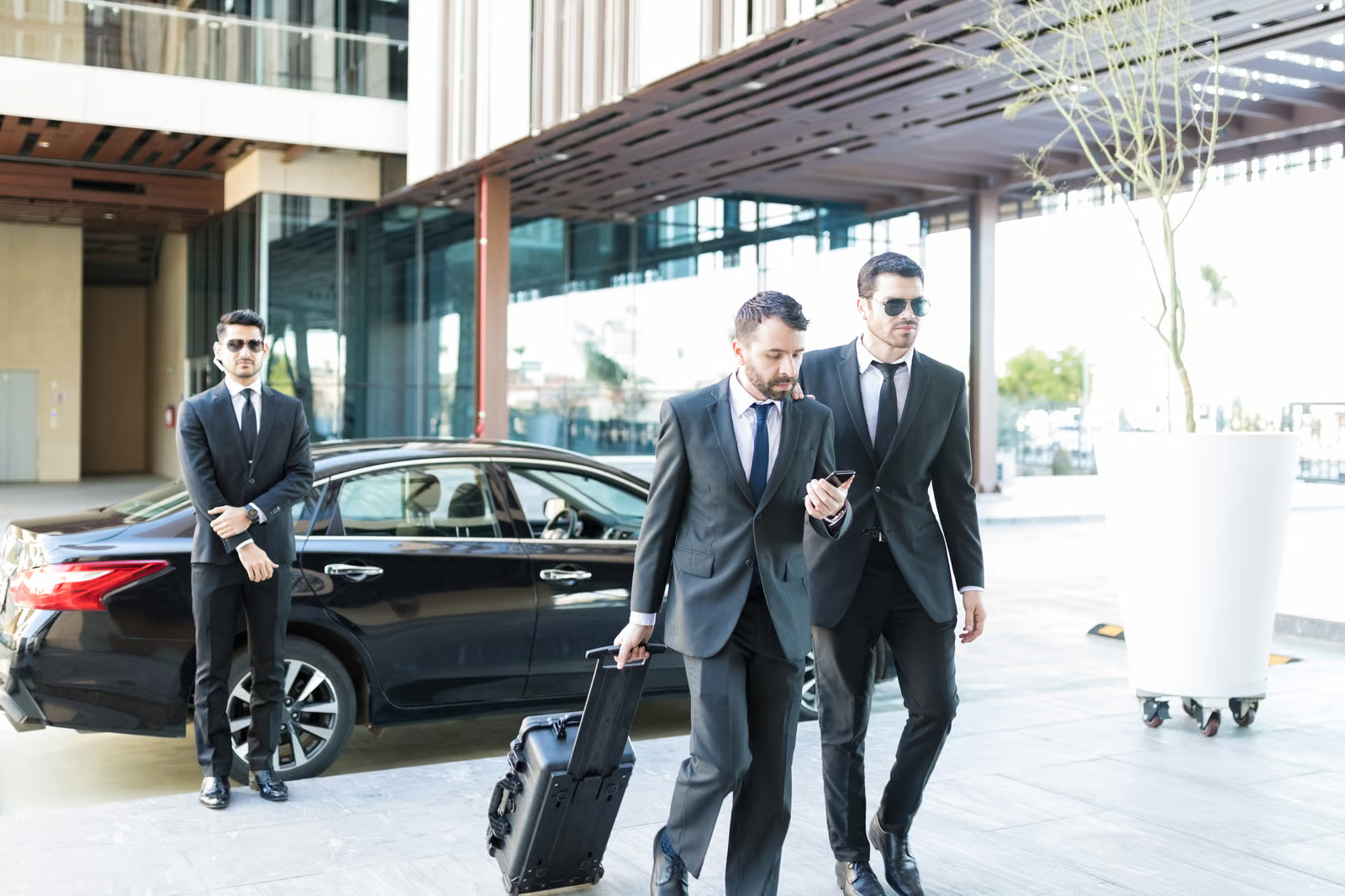 Executive mit Bodyguards und Gepäck am Fahrzeug