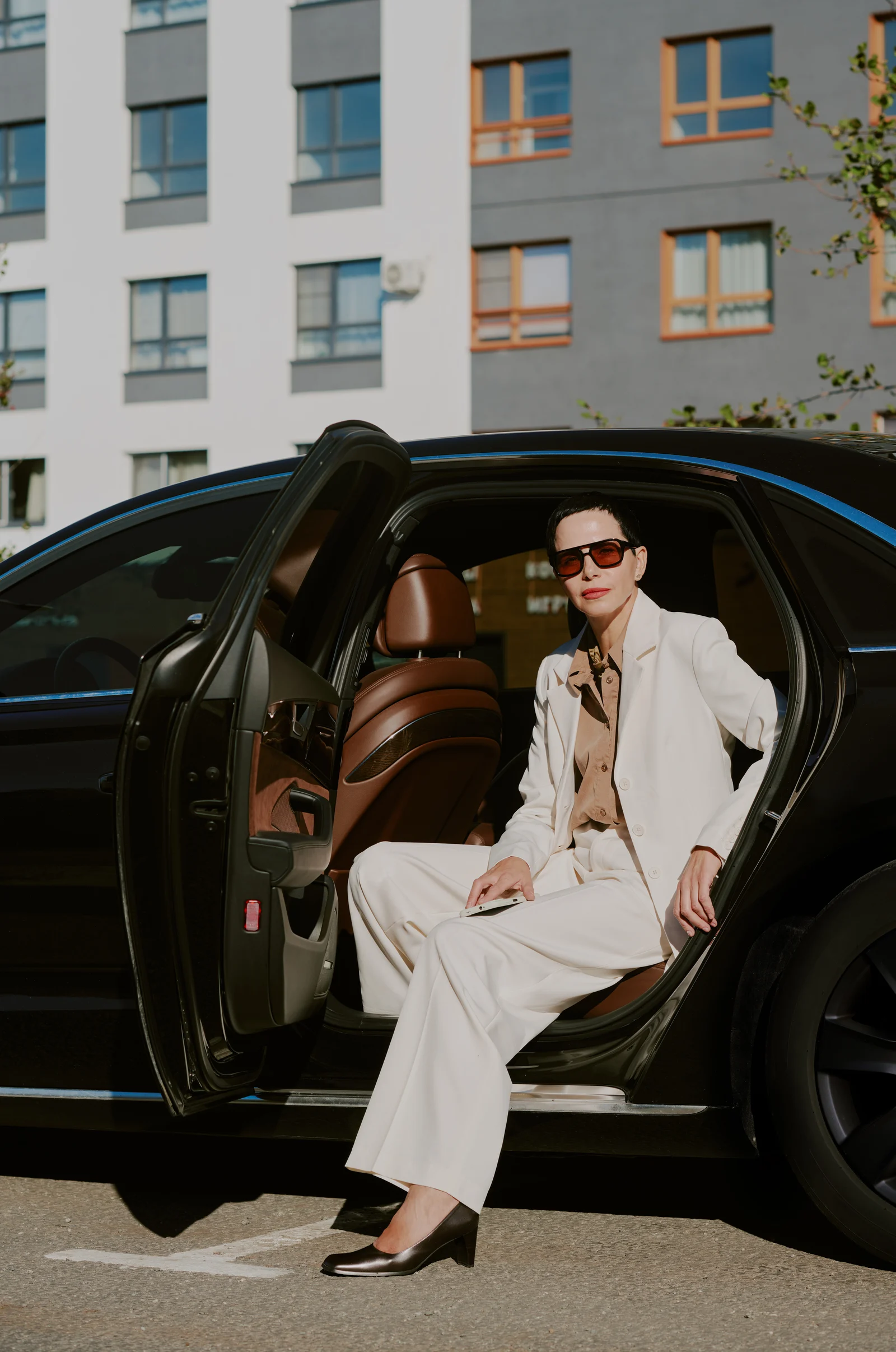 Flottenkoordination — Frau im cremefarbenen Anzug steigt aus Luxuslimousine (VIP-Flottenmandant)